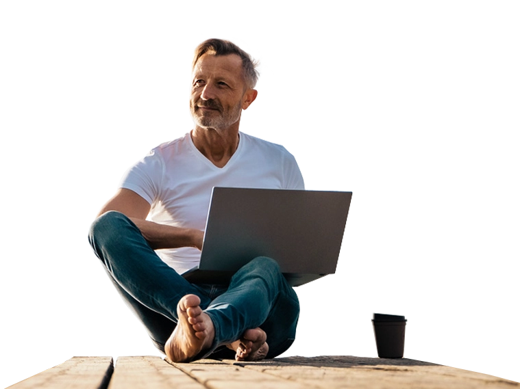 Mann sitzt mit Laptop auf einem Holzsteg und blickt in die Ferne